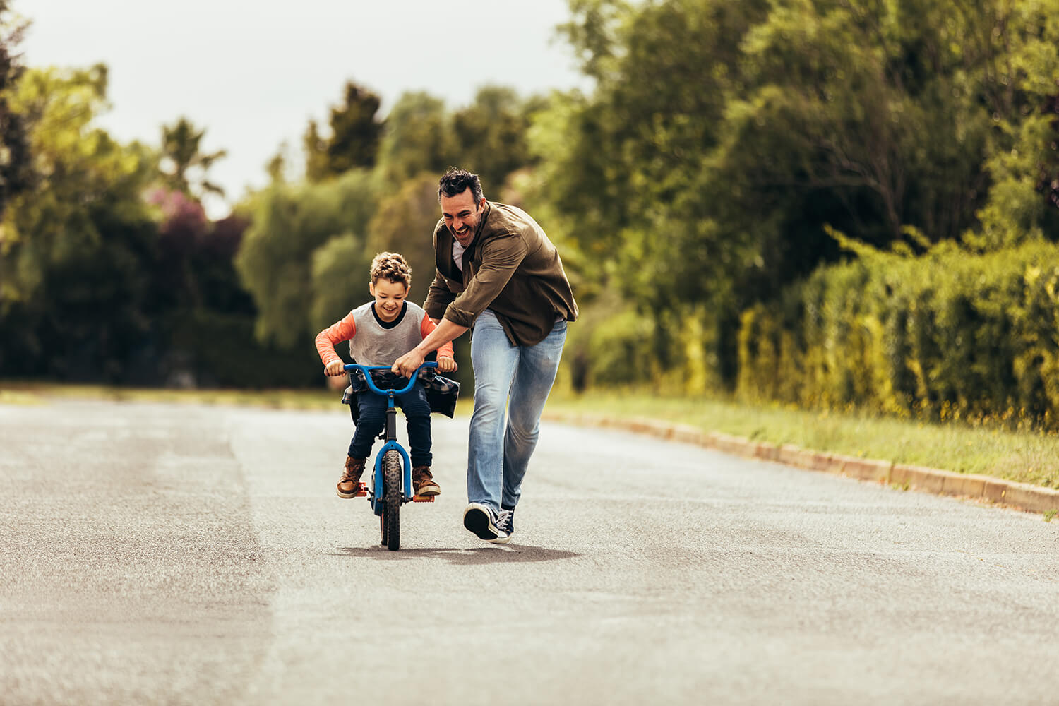 Smiling father teaching his young son to ride a bike on a quiet road, representing positive family moments in Knutsford.