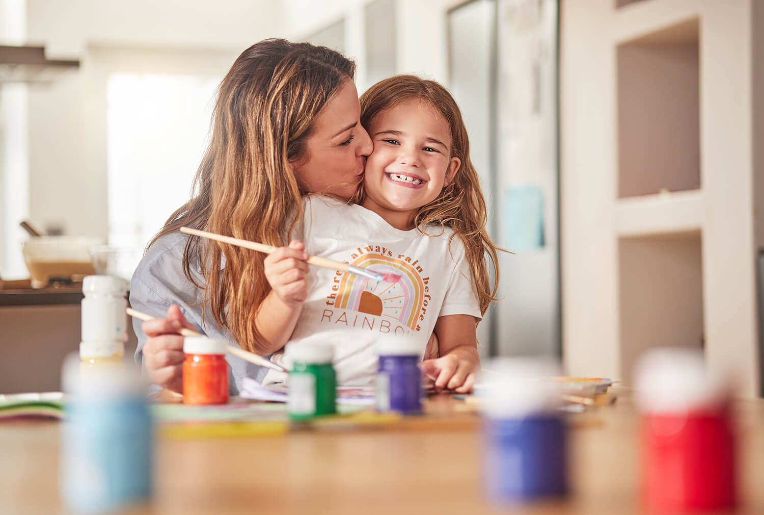 A mother kisses her daughter on the cheeks as they take part in a crafts activity.